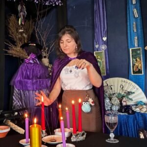 Mica Mihaylova em frente a um altar mágico com velas acesas de várias cores, incensos e objetos espirituais, vestida com capa roxa em ambiente azul ritualístico
