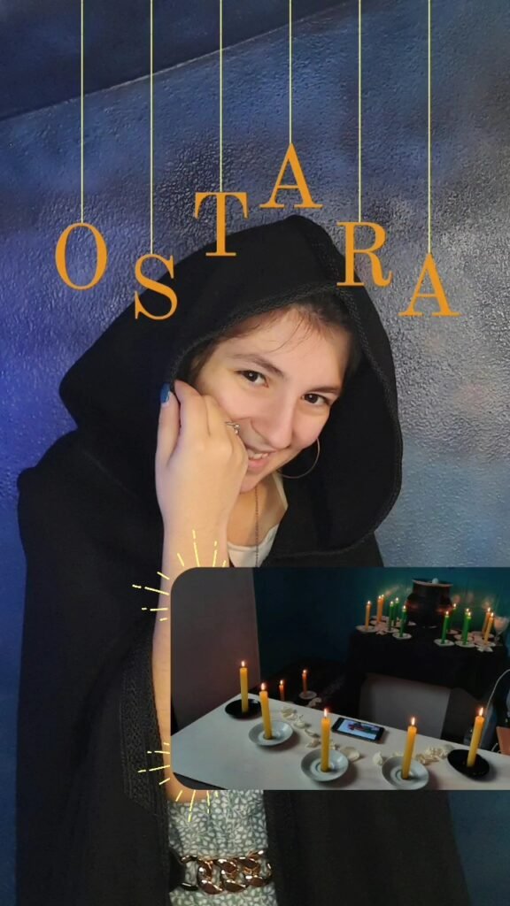 Imagem com Mica Mihaylova sorridente em frente a altar com velas acesas, vestida com capuz e fundo azul