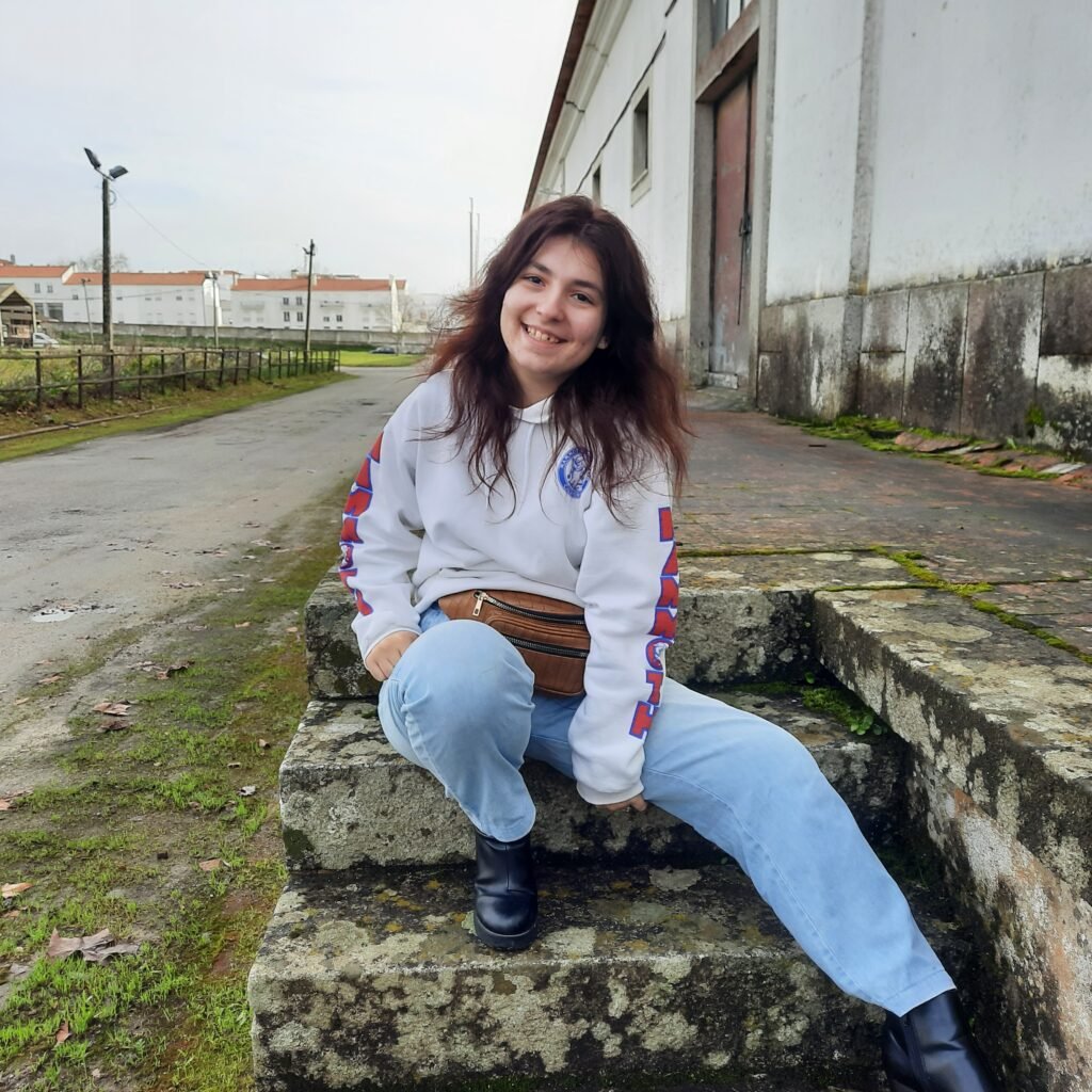 Mica Mihaylova sentada numa escada de pedra com hoodie branca e sorriso luminoso
