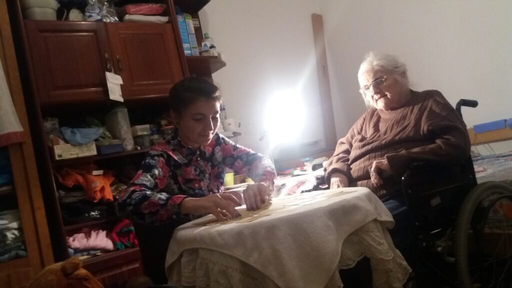 Mica Mihaylova ao lado da sua avó materna, sentadas à mesa com tecido claro, em ambiente acolhedor e familiar, partilhando um momento de tiragens